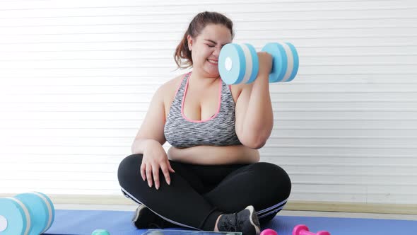 Stressed Asian woman overweight exercise by lifting dumbbells in living room at home