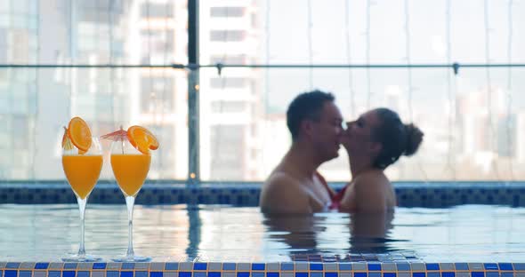 Blurry Couple Hugs and Kisses in Pool Water By Cocktails