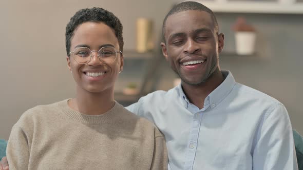 Portrait of Couple Smiling at Camera While Sitting on Sofa alt
