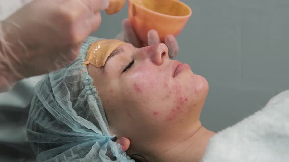 Female Cosmetologist Hands Apply an Orange Mask to the Client's Face