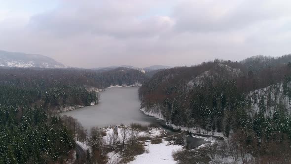 Aerial view of frozen lake surrounded with forest and fairy tale castle in the distance at winter alt