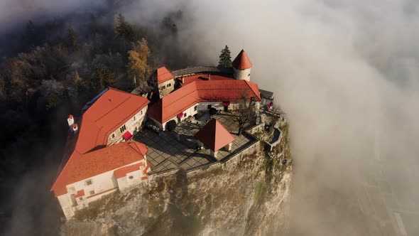 Golden hour aerial view over Bled castle, surrounded by morning clouds alt