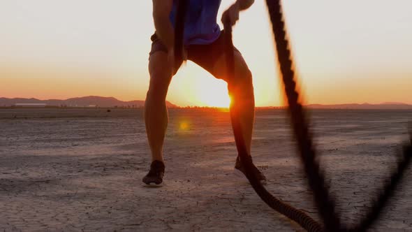 Athletic man working out with battle ropes on a dry lake at sunset alt