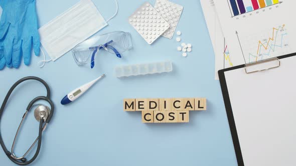 Phrase medical cost are made up of cubes on medical table by the hands of doctor, view from above alt