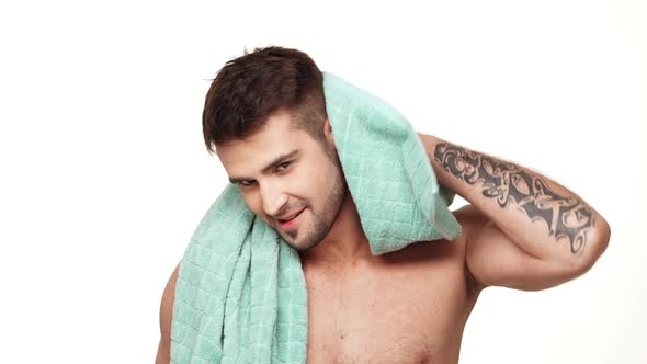 Positive Caucasian Topless Male with Tattoed Hand Wiping Head with a Towel Around His Neck Standing alt