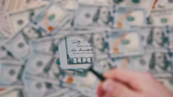 Lot of One Hundred Dollars Bills Inspecting Under Magnifying Glass alt