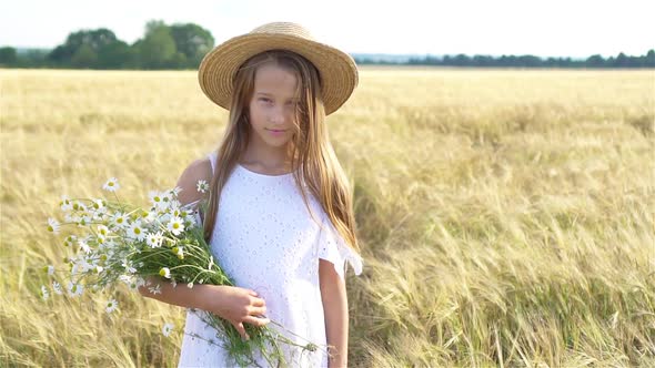 Happy Child in Wheat Field. Beautiful Girl in White Dress in a Straw Hat with Ripe Wheat in Hands