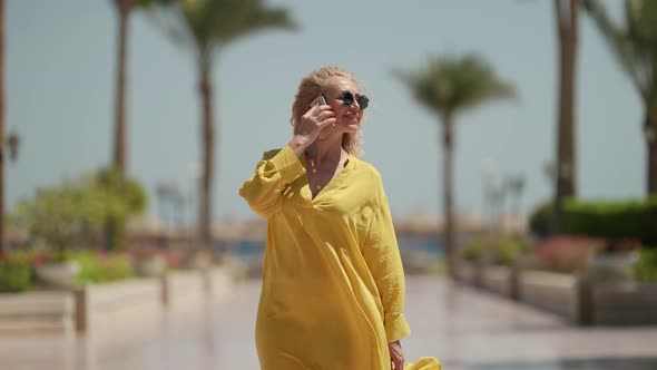 Rich Woman is Talking By Phone and Walking Outdoors in Summer in Tropical Country alt