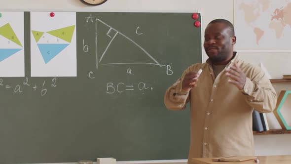 Black School Teacher Using Chalkboard and Explaining Lesson at Camera alt