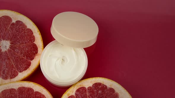 Cream Jar Near Pieces of Fresh Grapefruits in Water Splash on Red Background