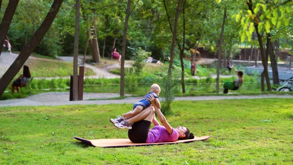 Young Woman Holding Baby and Working Out in Park alt