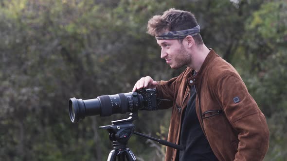 Young wildlife photographer with a DSLR tripod camera looking around. alt