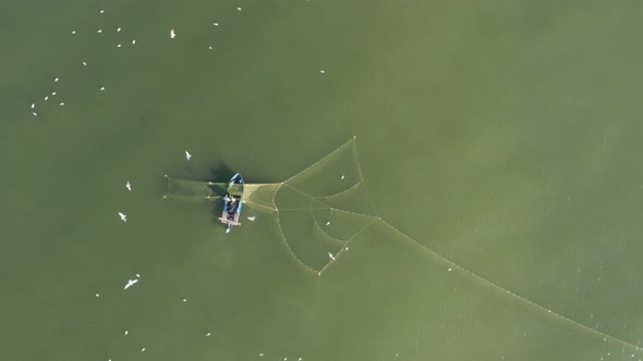 AERIAL: Fishermans Casting Nets in the Green Baltic Sea with Gulls Flying Around Searching for Fish alt