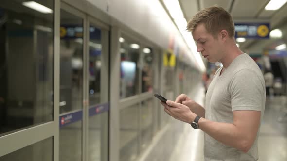 Profile View of Young Tourist Man Using Phone While Waiting for Train in Bangkok alt