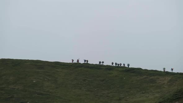 Group of Tourists with Hiking Backpacks Climbs the Mountain Range. Afar View alt