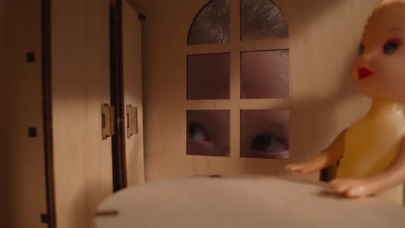 Interested Girl Peeks Into Window of Dollhouse in Dark Room alt