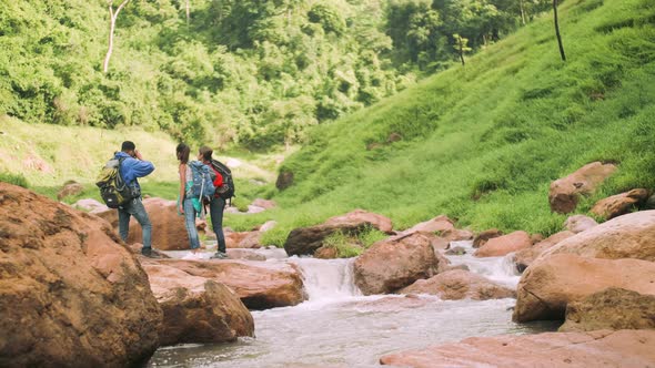 A group of trekkers with backpacks standing on the rock of a stream in a green valley. alt