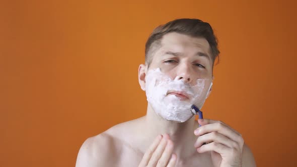 A Caucasian Man Shaves His Beard on Camera in a Studio on an Isolated Background