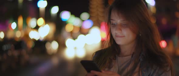 A young woman listening to the music on her phone in the middle of a street alt