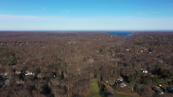 an aerial view over the edge of a pristine golf course, on a sunny day. Surrounding the golf course alt