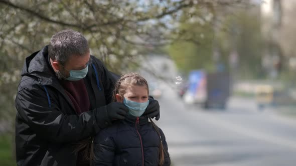 A Bearded Dad Adjusts His Daughter's Medical Mask on the Street of a European City . The Concept of