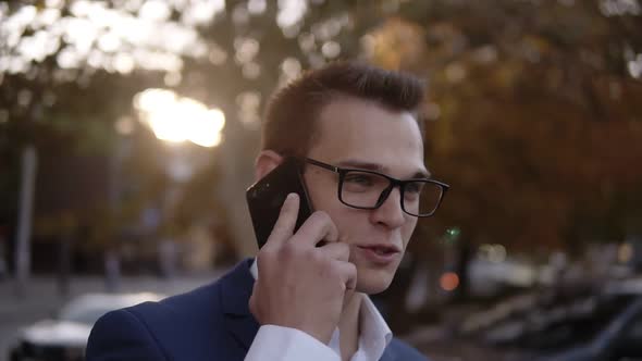 Portrait of Businessman in Stylish Glasses Talking on the Mobile Phone on Streets of Business alt