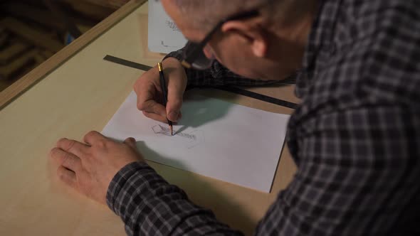 Aged Designer Draws a Sketch of Furniture Products on Paper at the Table