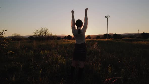 girl raises her hands in a field at sunset alt
