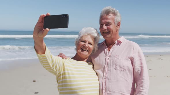Happy senior caucasian couple taking a selfie using smartphone on the beach alt