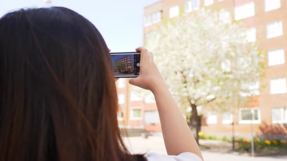 Back view of Asian Straight hair woman standing at a street and taking a photo of buildings view alt