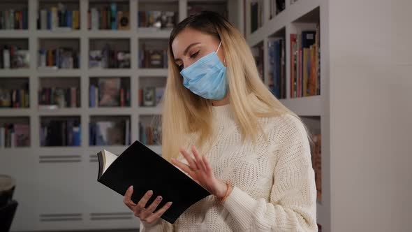 A Female Student in a Medical Mask on Her Face Reads a Book in the Library alt