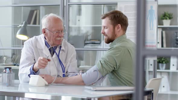 Senior Doctor Testing Blood Pressure of Young Male Patient alt