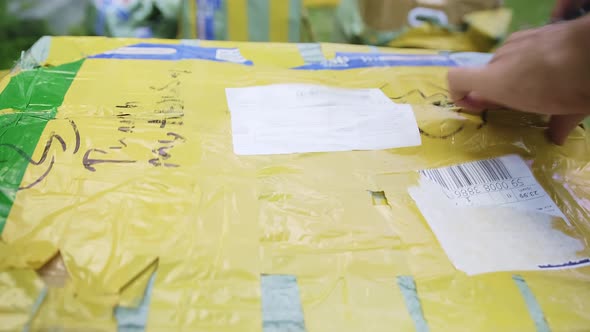 Closeup View of a Caucasian Man Trying to Open Taped Yellow and Brown Cardboard Parcel