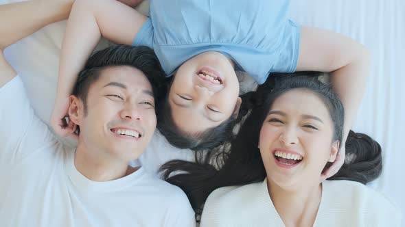 Happy Asian family mom dad and daughter child laying laugh smile on white soft bed alt