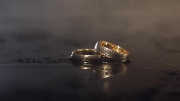 Wedding Rings on Dark Water Surface Shining with Light. Close Up Macro alt