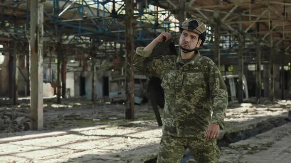 Man in Military Uniform Walking on Destroyed Plant alt