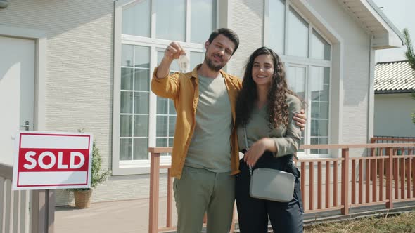 Portrait of Man and Woman New House Owners Standing Outdoors Holding Keys Hugging Smiling alt