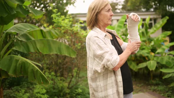 Senior Elderly Woman Doing Exercises and Gymnastic for Hand with Injury Broken Arm in Cast Outside