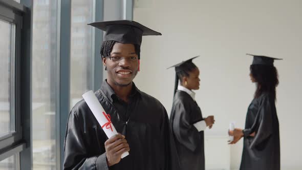 One Young AfricanAmerican Man Stands in the Foreground and Looks at the Camera with a Diploma in His alt