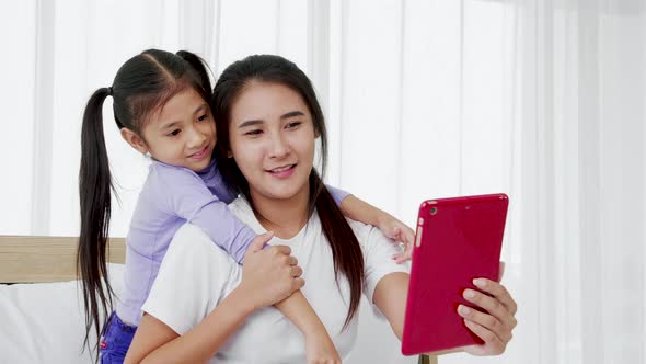 Happy parent mother and cute little child daughter looking at digital tablet at home