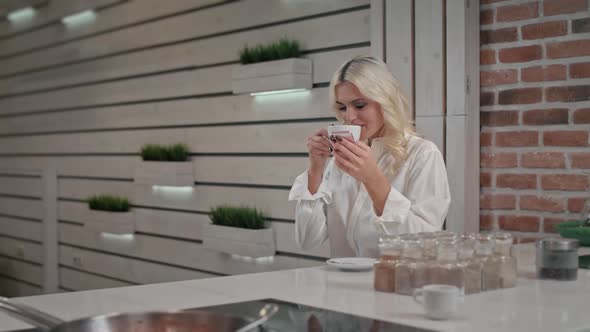 Portrait of Blond Woman Texting Message on Smartphone at Kitchen Smiles and Laughs