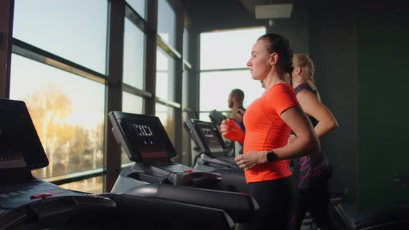 Cute Young Girl Running on a Treadmill in Front of Panoramic Windows in the Fitness Room. Gym with alt