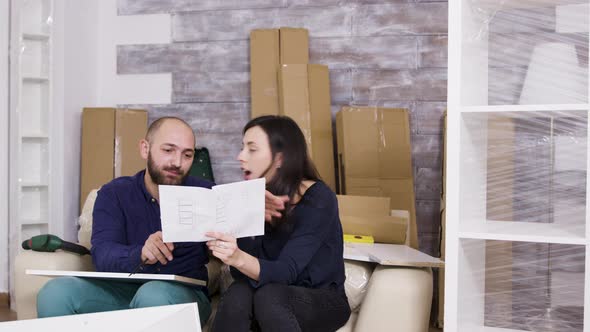 Girlfriend Hitting Boyfriend with Instructions While Assembling Furniture alt