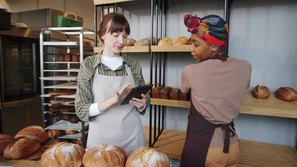 Two Multiethnic Women Using Tablet and Working in Bakery alt