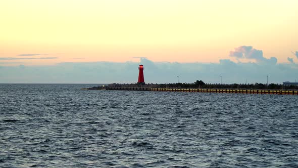 A red working lighthouse stands on the seashore near the water. Signals to nearby ships