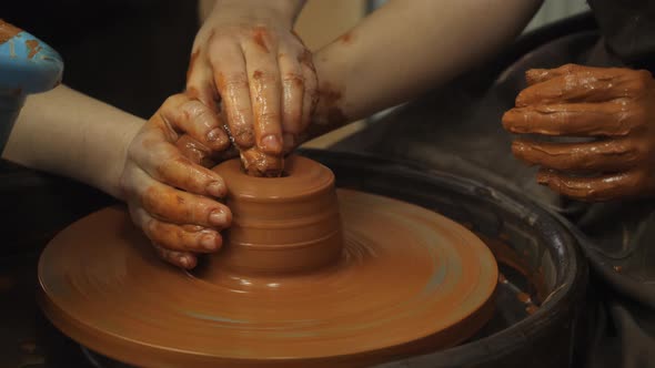 Closeup of Adult and Child's Dirty Hands Molding Clay Into Ceramic Pot