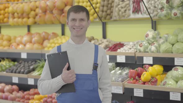 Portrait of Young Brunette Caucasian Man in Uniform Posing in Grocery Shop. Positive Employee alt