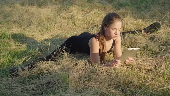 Wide Shot of Young Beautiful Absorbed Woman Sitting in Split and Using Tablet Outdoors. Portrait of alt