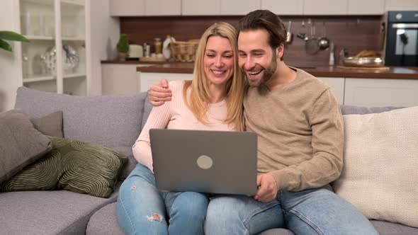 Happy Couple Using Laptop for Video Connection to Friends or Family Looking at the Webcam