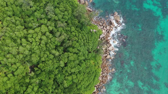 Drone field of view of turquoise blue waters following coastline of green forest Praslin Seychelles.